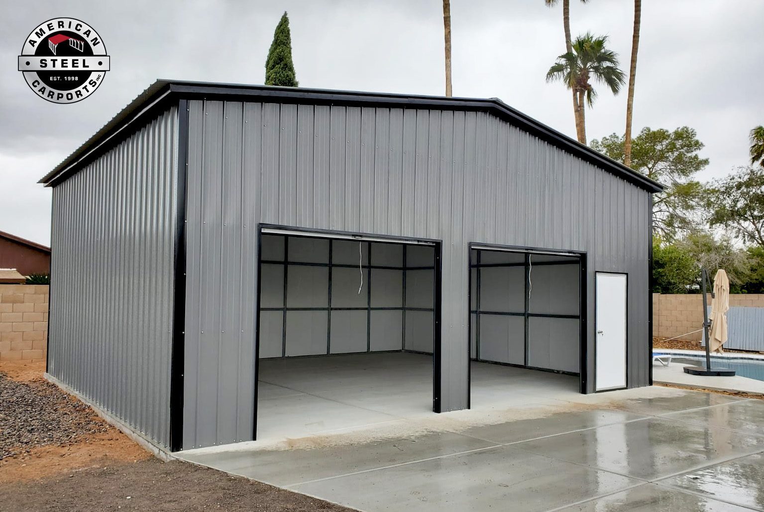 Gray steel garage with open bays beside a backyard pool