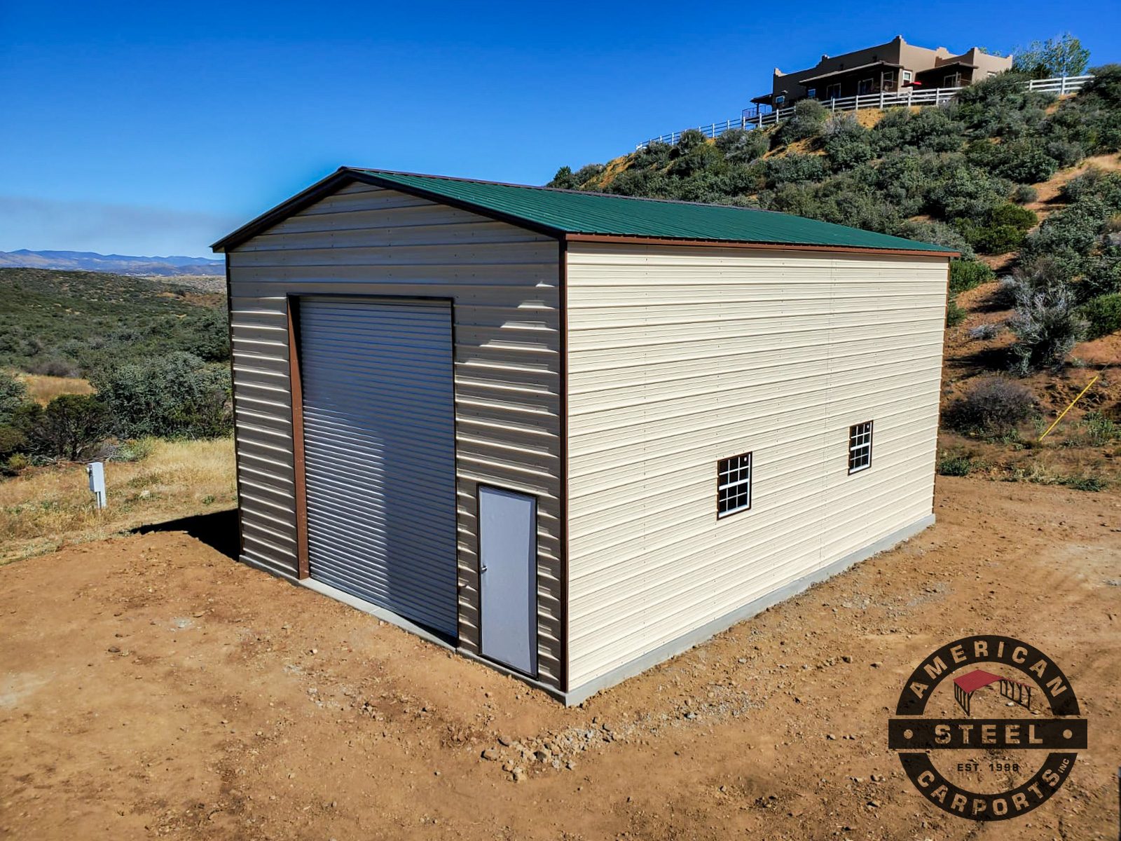 Tall tan steel workshop with green roof on hillside lot